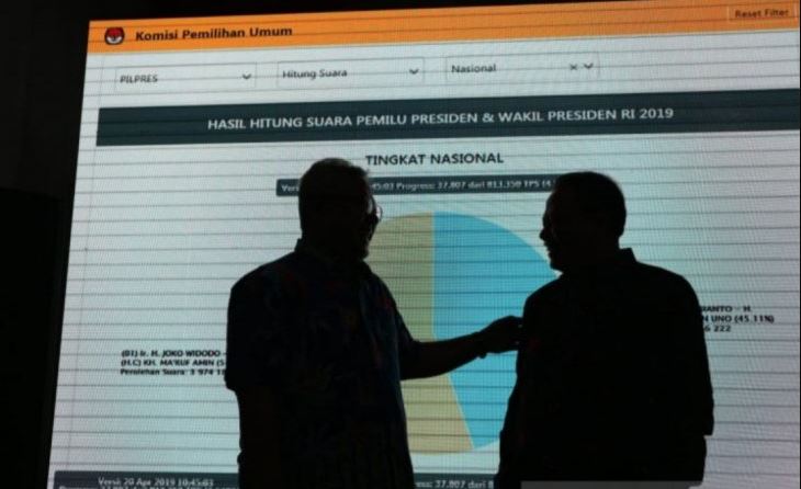 Siluet Ketua KPU RI Arief Budiman (kiri) dan Ketua Bawaslu RI Abhan Misbah (kanan) di depan layar monitor yang menampilkan hasil hitung suara Pilpres 2019 di kantor KPU RI, Jakarta, Sabtu (20/4/2019)