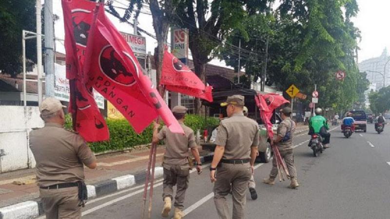 Satuan Polisi Pamong Praja (Satpol PP) kecamatan Cempaka Putih menurunkan atribut bendera- bendera partai milik PDI Perjuangan. (Tempo.co)