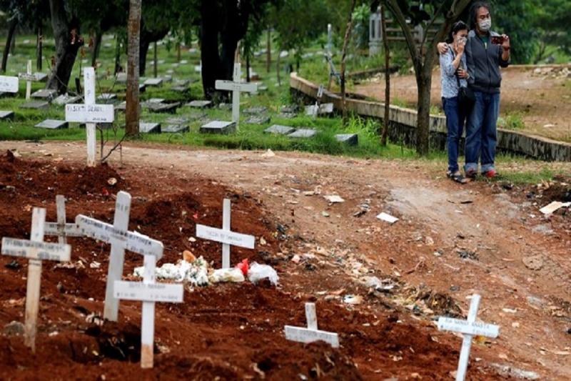 Kerabat yang memakai masker wajah berdiri di sebelah kuburan korban COVID-19 di sebuah area pemakaman yang disediakan oleh pemerintah di Jakarta, Indonesia, 3 April 2020. Foto/REUTERS/Willy Kurniawan
