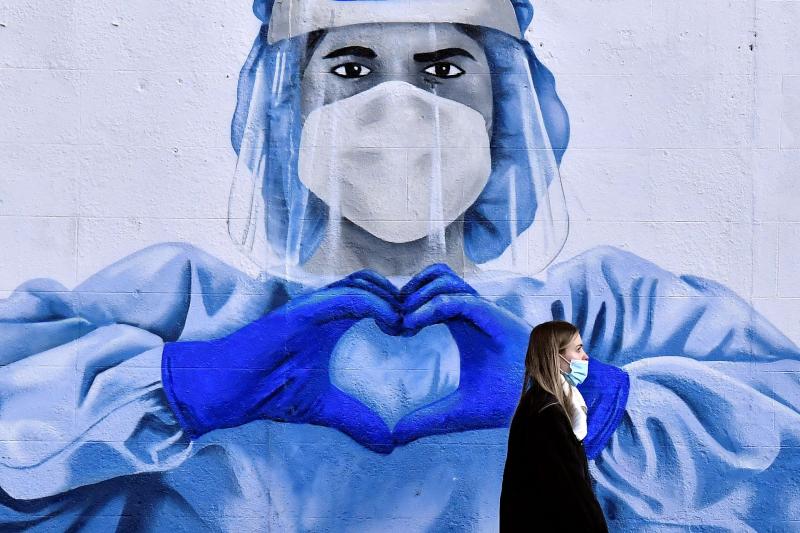 Seorang wanita berjalan melintasi mural tenaga kesehatan ketika pandemi COVID-19 (Reuters)