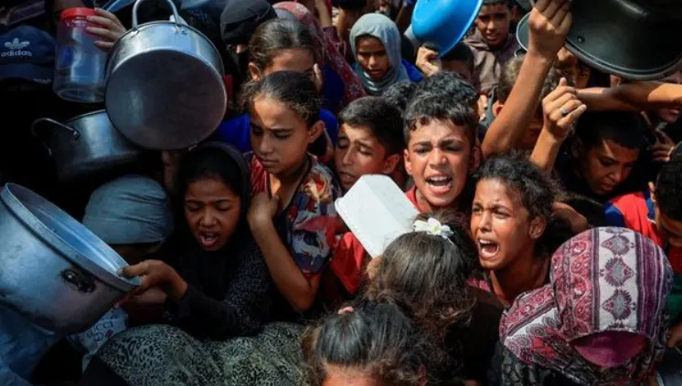 Warga Pelstina tengah menanti pembagian makanan dari Dapur Umum di Khan Younis, Gaza, Kamis (21/8). (Reuters via Detik)