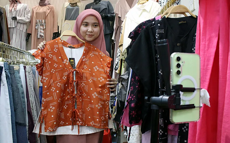 Pedagang menawarkan dagangan melalui siaran langsung pada Hari Belanja Nasional (Harbolnas) 12.12 di kiosnya, Jakarta, Jumat, (12/12/2025). Pemerintah menargetkan nilai transaksi Hari Belanja Online Nasional (Harbolnas) 2025 mencapai Rp 35 triliun selama periode 10–16 Desember. Tahun 2025, fokus utama kampanye belanja ini diarahkan pada peningkatan pembelian produk Usaha Mikro, Kecil, dan Menengah (UMKM) lokal. Robinsar Nainggolan